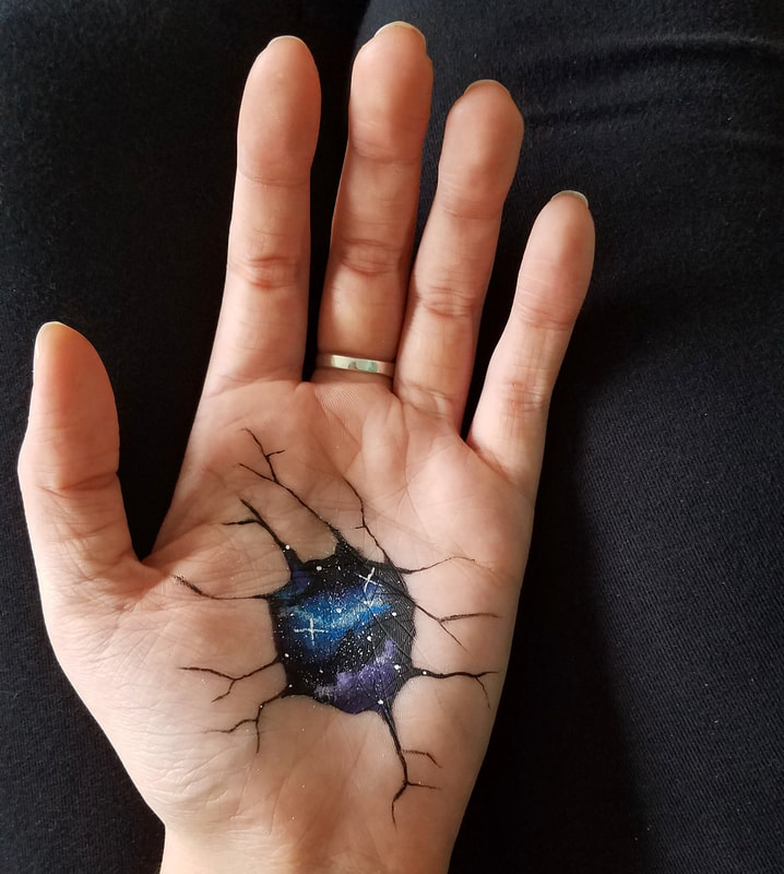 Photograph of a hand with a small galaxy painted into the palm