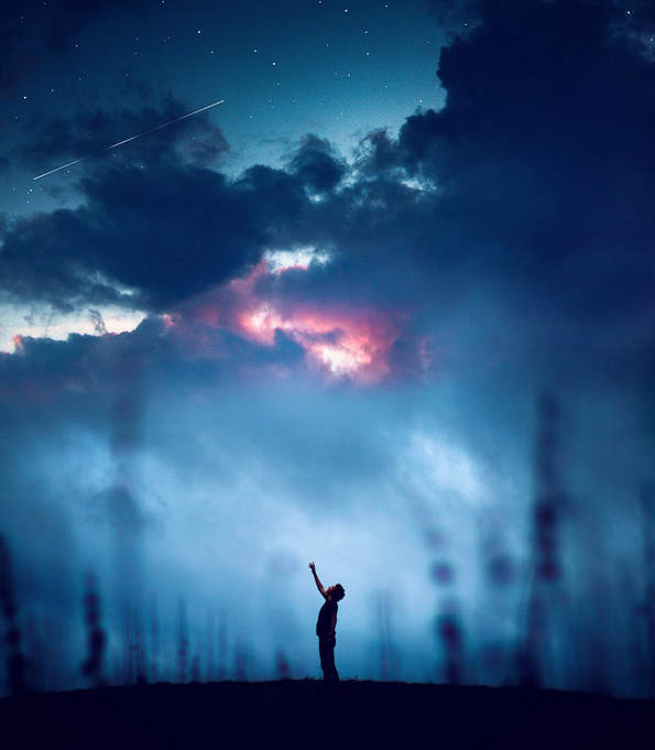 Photograph of a boy reaching toward a dark blue sky and stars